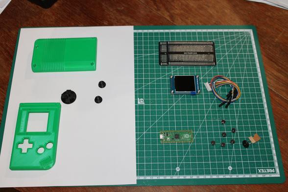 Parts laid out for the Pico Game Boy - a 3d printed case and buttons, prototyping board, a screen and connection cable, a Raspberry Pi Pico, some buttons, and a piezo buzzer.