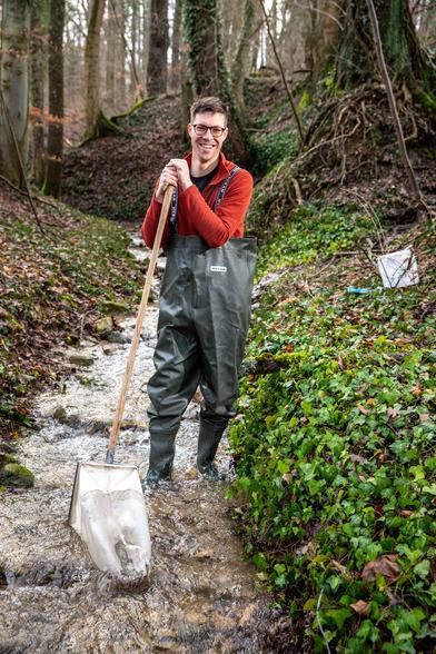 Portrait of Roman Alther with freshwater stream sampling equipment, standing in a small creek