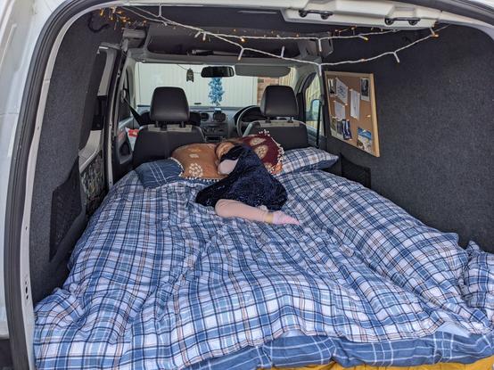 Bed made inside a converted small van, young child sleeping on it fairy lights just in view.