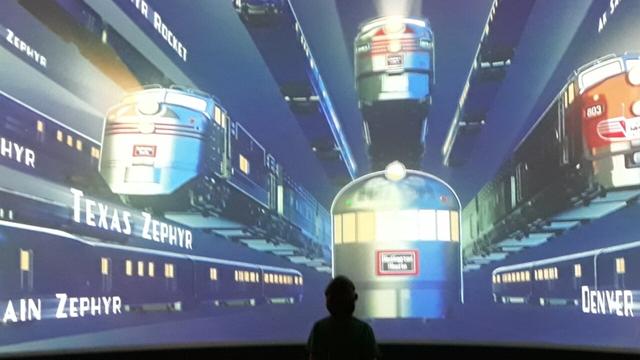A child stands in front of a screen showing Streamliner trains