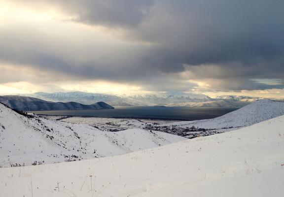 Great Prespa Lake set in a bowl of mountains covered by snow, with three countries show in the image: the foreground hills are in Greece, the mountains at the centre-back are in Albania, and the mountains at the far-back on the right are in North Macedonia.