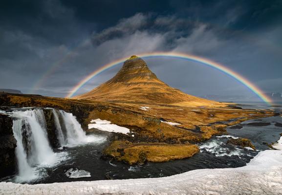 Mountain with a rainbow over it and a waterfall in the foreground.