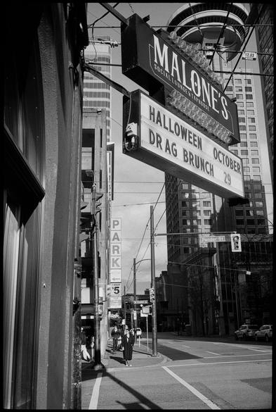 Bar sign and Vancouver skyline looms at intersection cast with long shadows
