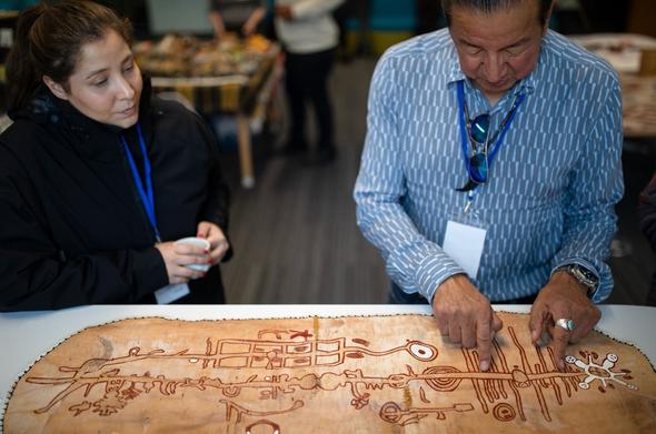 a participant and a Philip Cote, an Indigenous artist, examine a Birchbark scroll