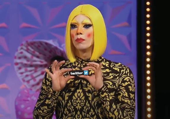 A screen grab from the show RuPauls Drag Race; a drag queen (Pangina Heals) is holding up an elimination lipstick. The lipstick has been photo edited to have the word Twitter written on it.