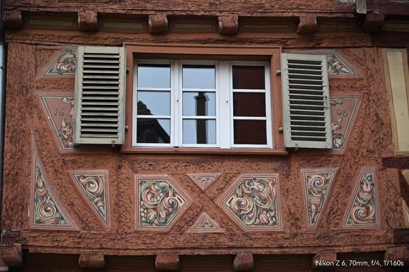 Dreiflügeliges Sprossenfenster mit Fensterläden in einer reich mit floralen Motiven ausgemalten und geschnitztem Fachwerkhaus im nördlichen Elsass (Bouxwiller)