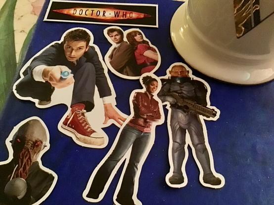 A number of Doctor Who fridge magnets spread out on a blue background beside a large mug. All are from the David Tennant era of the show, and include the Doctor, the Doctor and Donna, Martha, an Ood, a Sontaran, and the old series logo.