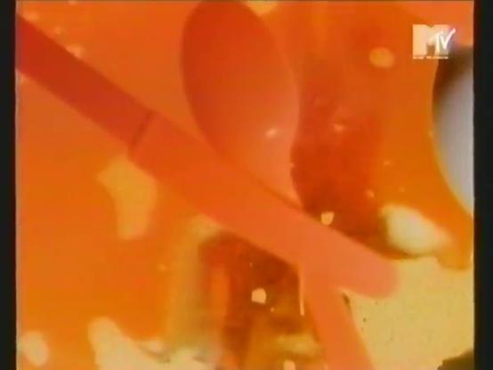 Kuvakaappaus VHS-nauhalta: aterimia tiskivedessä. Kaikki oranssinpunaista; vain oikealla laidalla kanamunanpuolikkaan muotoinen valkea alue. Oikeassa yläkulmassa MTV:n (Music Television) logo.