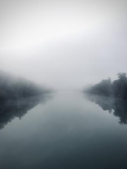 View upstream of the Rhine rive disapearing into the fog. Trees on both sides of the river.

Blick flussaufwärts auf den Rhein wie er vom Nebel verschluckt wird. Beidseitig des Flusses sind Bäume.