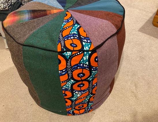 A range of triangular fabric pieces are joined to create a circular patchwork top to a 60cm tall cylindrical pouf. The fabrics are a mix of wool and brushed cotton and African wax print.