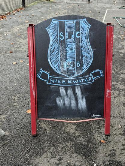 Sheerwater's crest in blue chalk on a blackboard advertising the bar open, signed by Banksy. 

We suspect humour.