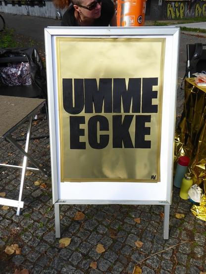 Ein Aufsteller mit einem goldenen Plakat und der Aufschrift "Umme Ecke"