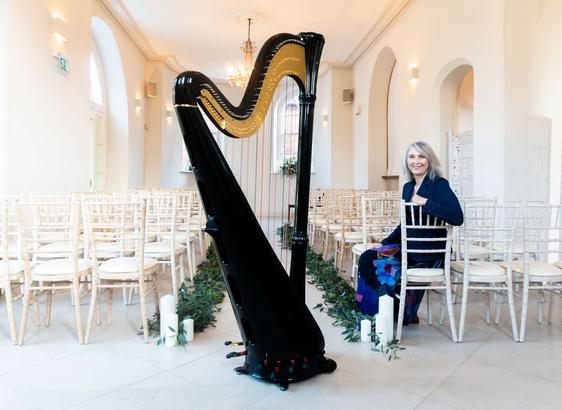 A large black harp at the back of a garden room where a wedding ceremony is about to take place.