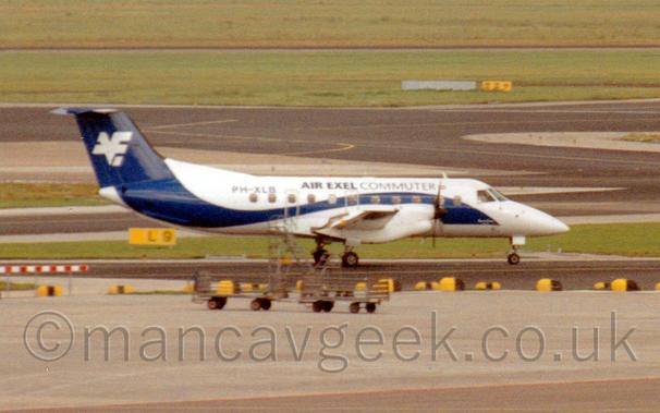 White propellor airliner with a swooping blue line extending along the length of the fuselage and up the tail.
The fuselage has the words "Air Exel Commuter".