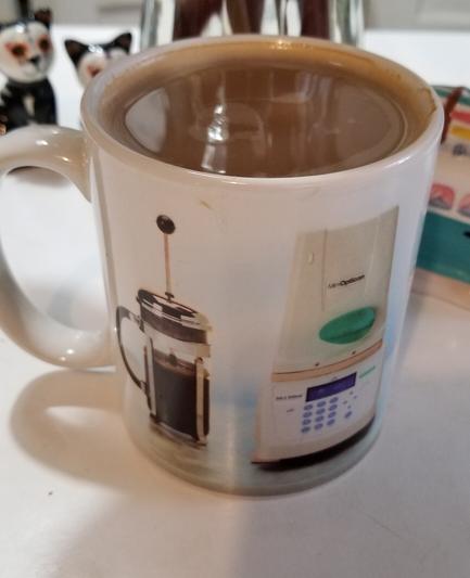 Coffee mug with a picture of a French press on the left and PCR machine on the right.
