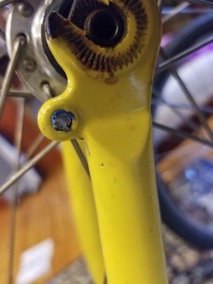 A broken screw with blue Loctite is visible in an eyelet near the wheel of a yellow bicycle.