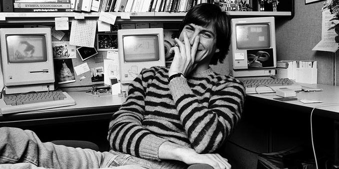 Young Steve Jobs smiling at desk in early Apple days