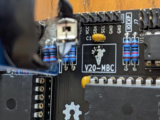 Closeup view from above of a black printed circuit board with black chips. The board has as a logo a white line drawing of a two-flavor ice cream cone. The label "V20-MBC" is below the drawing.