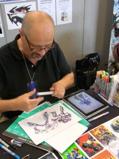 Honestly, if there weren't the bits of paper with the name Lee Sullivan written on them behind him on the wall, I'd have forgotten the name by now.

He has some Transformers bit of art in front of him, drawn for someone else, and some of the postcards he was selling at the front. I can't for the life of me remember if I got something done by him or not.