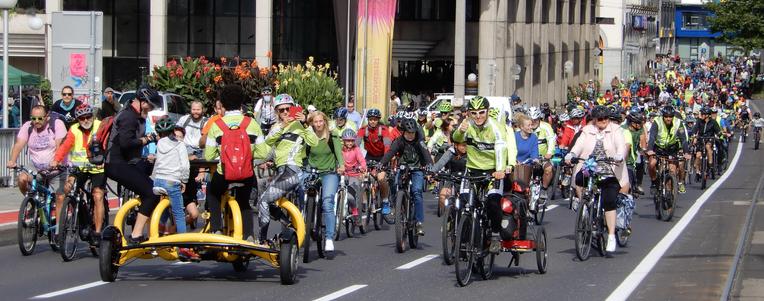 Viele RadfahrerInnen radeln im Konvoi auf einer großen breiten Straße bei einer Rad-Parade. Die Masse erstreckt sich über den ganzen Bildausschnitt. Auch ein sogenanntes Konferenzfahrrad ist dabei, auf dem mehrere Personen im Kreis angeordnet in die Pedale treten können.