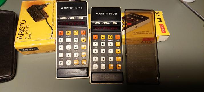 Two Aristo M75 calculators propped up on an Aristo box. Matching power supply next to them.