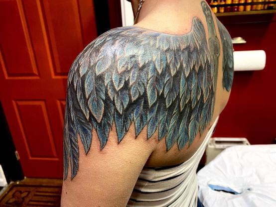 Photo of a raven wing tattoo wrapping around the shoulder, in blue and black