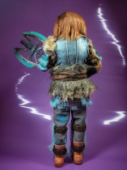 A photo of a customised doll. Representing the character of Karvanista from Doctor Who. He is a humanoid dog. He wears armour and furs. Back view.