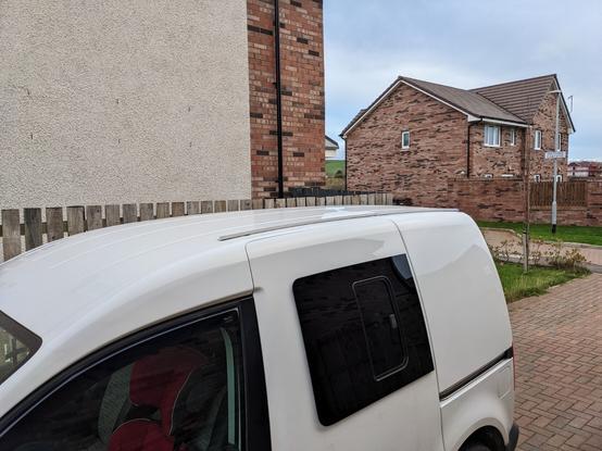 Side view of a white VW Caddy van with an after market side window installed and showing a simple awning rail installed along the roof