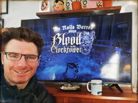 A blown out photograph of myself smiling next to the television with the title “No Rolls Barred plays Blood On The Clocktower.” Nearby is a my cup of coffee.