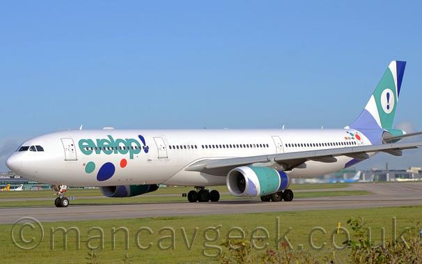 Large white two engined jet airliner with green "Evelop!" titles and green, red, and blue splotches on the fuselage, and blue, green, and purple splotches on the tail and engines.
