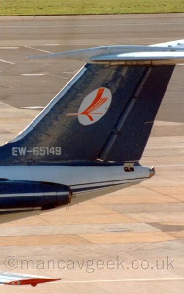 Close up on the tail of a T-tailed twin engined jet airliner.
The fuselage is white, the back of the engines are visible, and are a deep blue with a white stripe.
The tail is the same deep blue as the engines, with a white oval in the middle, overlayed with the stylised inmage of a red flying bird.
The tail aslo has the registration painted on in white, EW-65419.