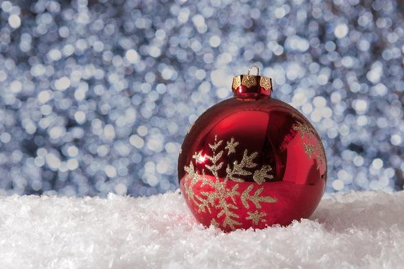 Shiny red ornament with glittery gold snowflake sitting on crystalline snow with a blue background of falling snow.