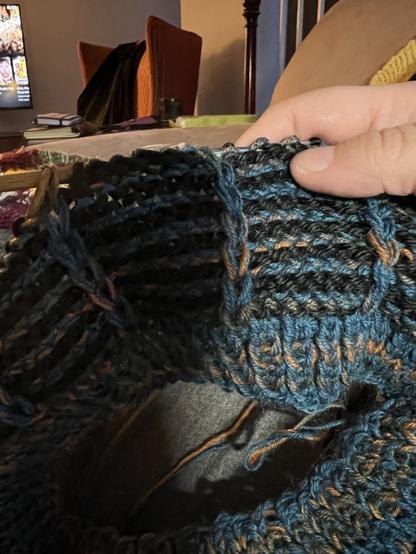 A black and blue stripped hat being knit with slipped stitch vertical details and a ribbed brim.