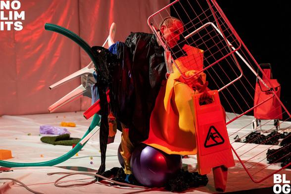 Eine Person kniet in einem Haufen von Dingen: ein Wäscheständer, eine gelbe Decke, ein Ball, ein weißer Plastikstuhl. Rotes Licht.
