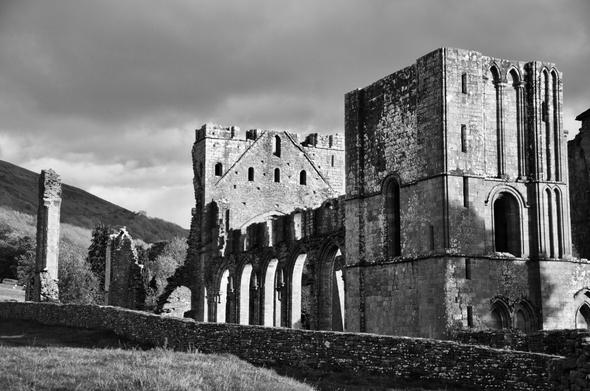Black & white image of ruined priory with hills and dark skies in background