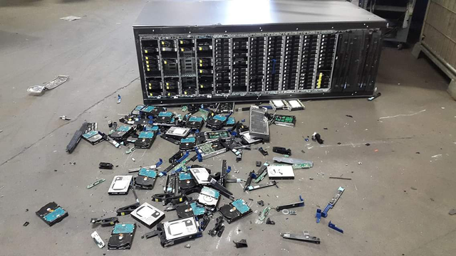 photograph of a server that has seemingly been dropped, with parts of hard disks and hard drive cages lying around in front of it