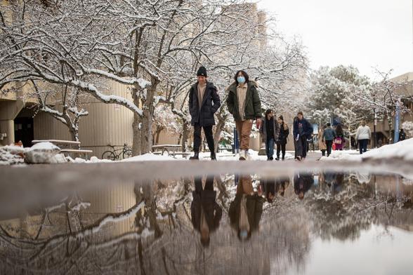 People walk on UTM campus. They are reflected in a puddle of melting snow.