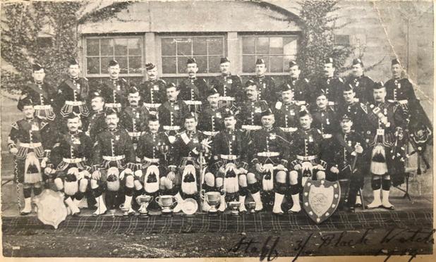 3 rows of officers and men in kilts, the front most seated.