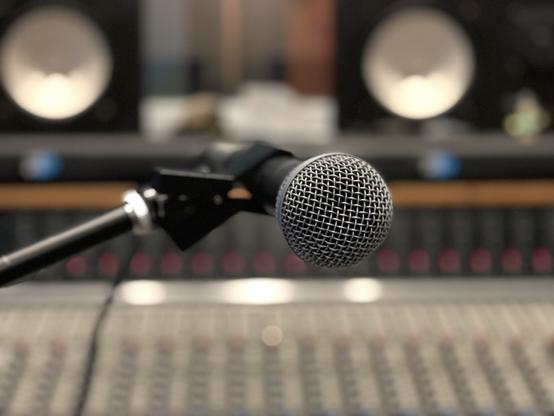 Shure SM58 microphone against a soft focus background of a mixing console and studio speakers.