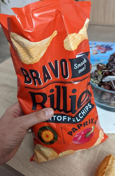 Eine frisch geöffnete Tüte Paprikachips. Der Daumen markiert die Füllhöhe ab Werk, welche bei circa einem Drittel der Tüte liegt.