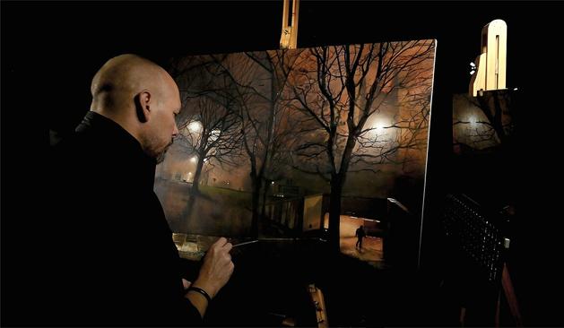 This photo shows an image of a cityscape painting which is nearing being finished. The view is of St Mary's church, here in Sheffield as seen from inside the nearby roundabout. The picture shows a church with a street light glow where the clock face should be. Silhouettes of trees fill the scene and a bank of grass leads up to the side of the unseen roundabout road. A small man can be seen walking into an entrance to an underpass. The whole scene has a feeling of winter and cold despite the warm sodium lit sky

This layer is an underpainting layer. All the forms have now been defined and it's very clear a night scene is shown. Everything has been further modelled and qualities of complex colour and form have come into the painting.  Andy can be seen in profile working on details in the foreground of the painting.