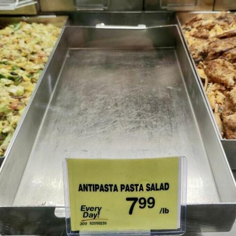Sign reading “Antipasta Pasta Salad $7.99” on empty tray at market.