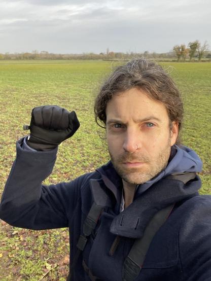 A man with a ponytail taking a selfie with a raised, gloved fist, in an attempt to look convincingly trade-uniony