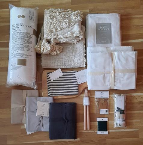 A flat-lay style assembling of various home decor items bought at H&M Home, from curtains over pillow cases to candles, in largely muted colours.