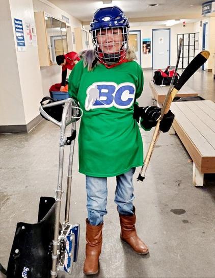Me in my green BC hockey jersey & helmet & gloves. Holding a hockey sledge on left & sledge sticks on the left.