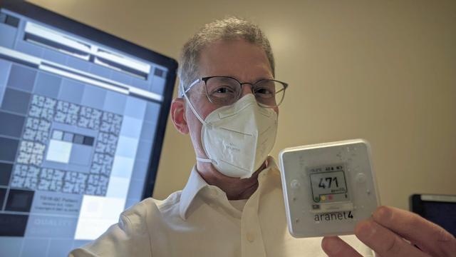 Self-portrait of a man with glasses and a white collared shirt wearing an Eclipse Arc respirator holding a CO2 meter displaying 471 ppm. In the background is a DICOM test image on a radiology monitor.