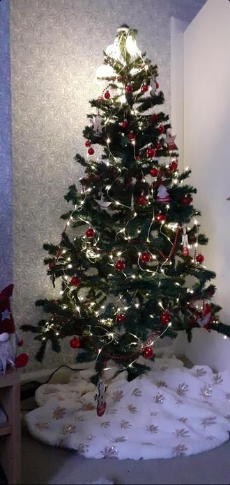 Artificial Christmas tree decorated with white lights and red baubles. It still needs a star on top.