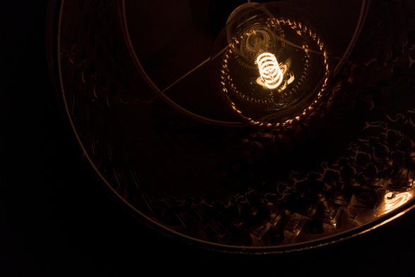 A ceiling light made from copper-like reflective material. The spiralling filament of the light bulb is clearly visible as it glows in the otherwise dark image.