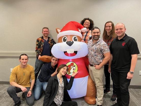 Group of seven men and a woman around an inflatable Buc-ee beaver, smiling and posing