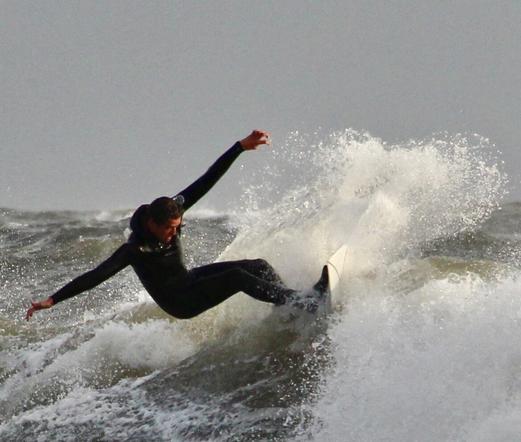 Wet-suited surfer riding the top of a wave at Langland Bay, Gower